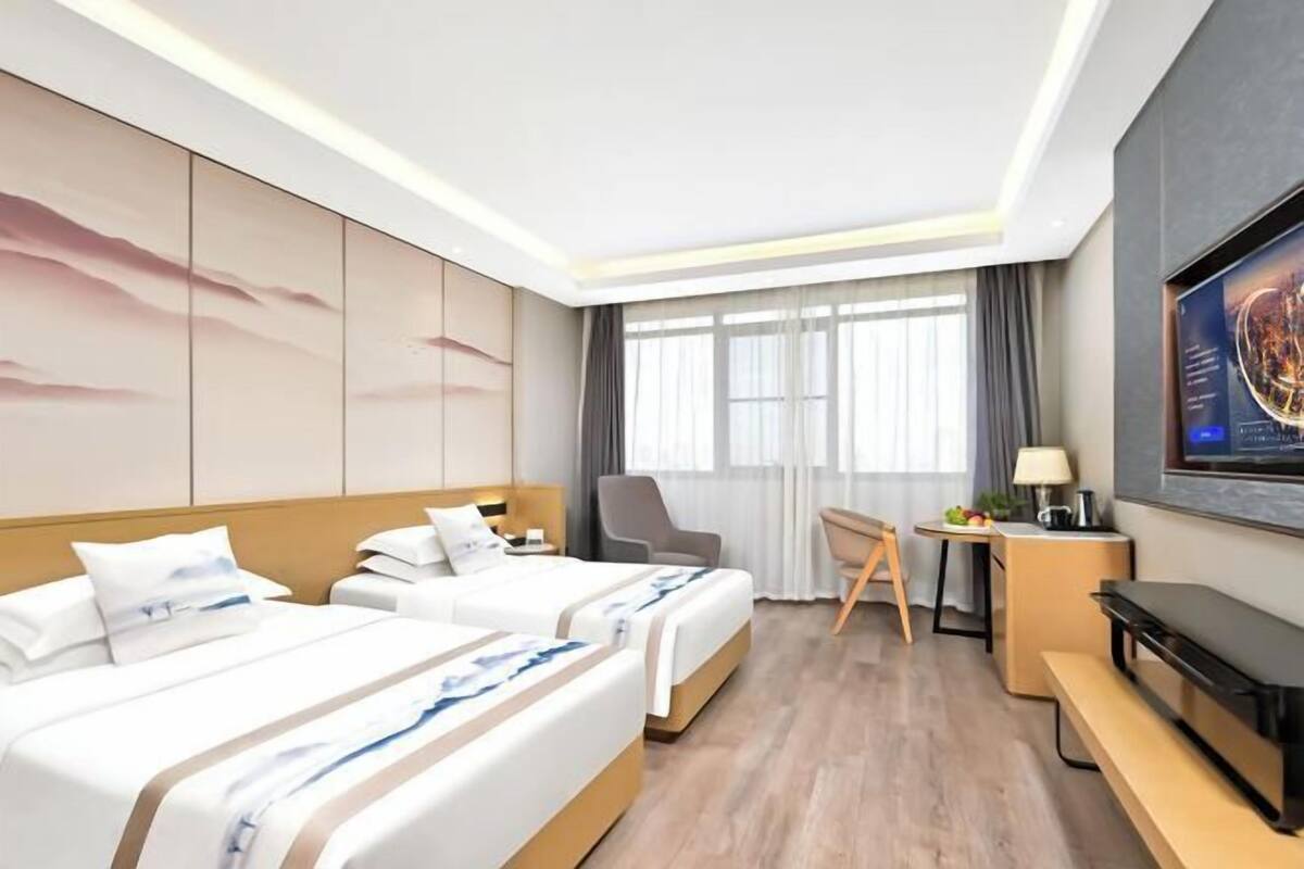 A hotel room with two beds, a desk, a chair, a TV, and a large window.