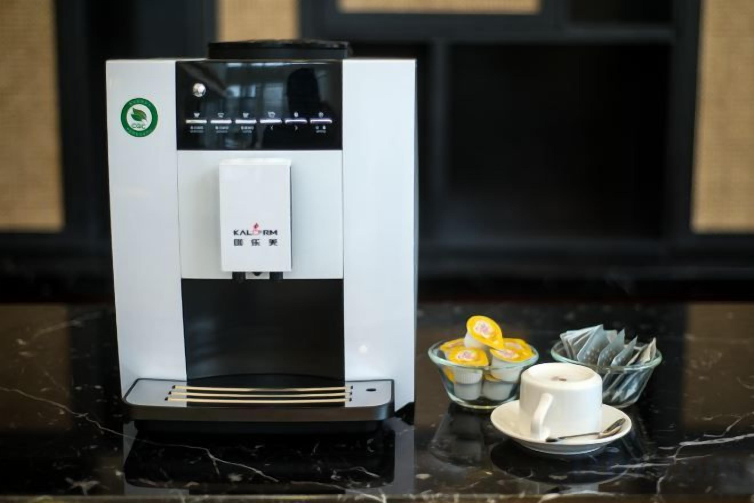 A coffee machine with a digital display, a cup, and a small bowl with lemon slices on a marble countertop.