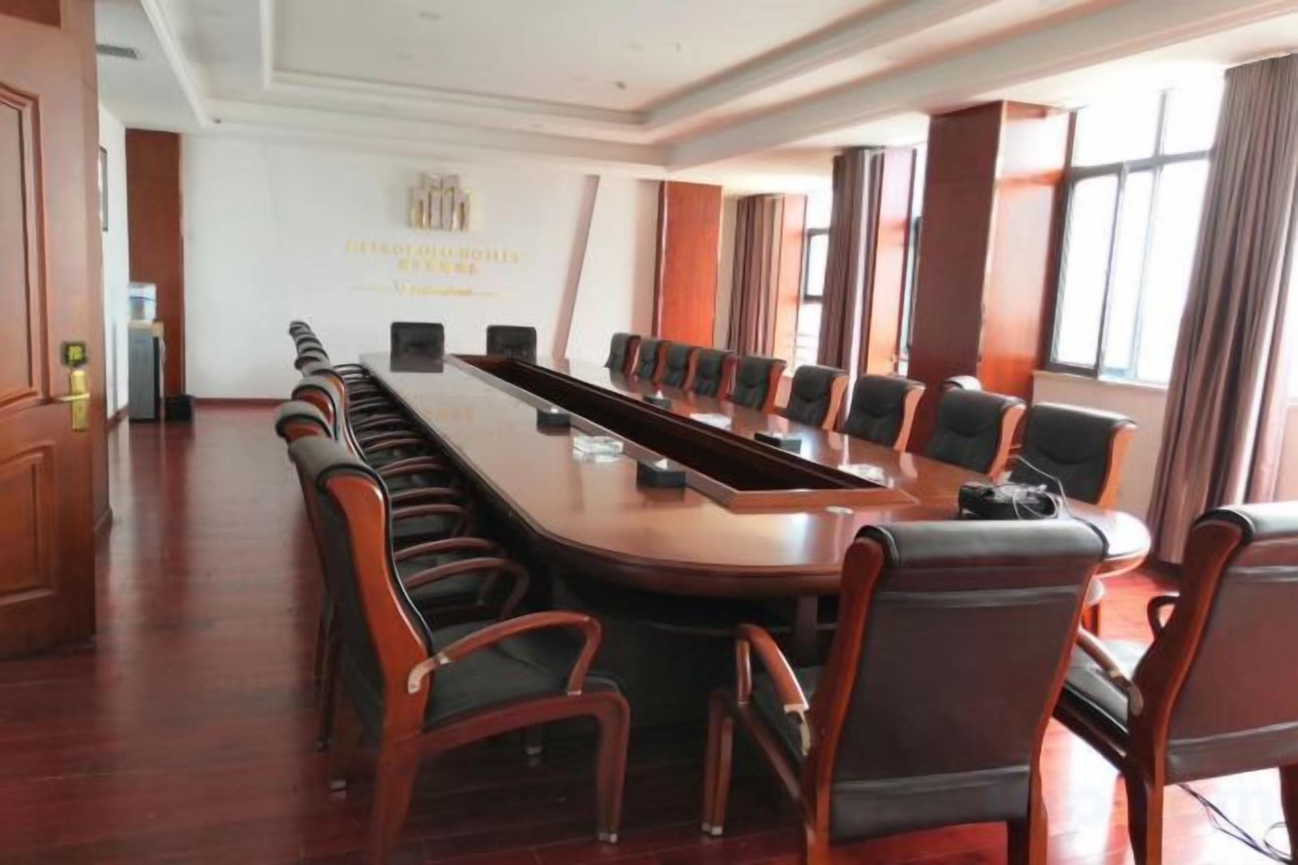 Un salón de conferencias con una larga mesa, sillas, ventanas amplias y una pizarra.