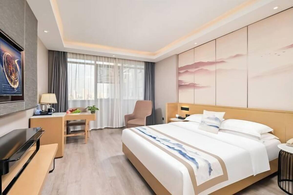 A hotel room with a bed, a desk, a chair, a TV, and a painting on the wall.