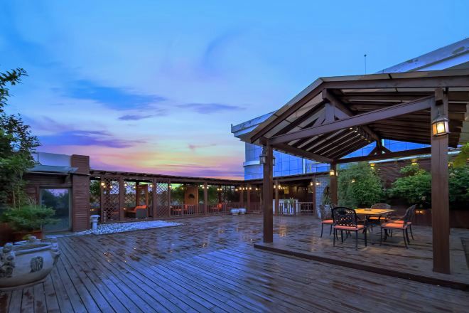 Une terrasse extérieure en bois, dotée d’un espace salon couvert et offrant une vue sur le ciel.