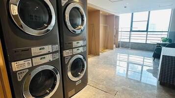 A laundry room with stacked washers and dryers, a tiled floor, and a view of the city through large windows.