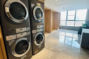 A laundry room with stacked washers and dryers, a tiled floor, and a view of the city through large windows. - Jinjiang Hotel International Hotel (Feng County)