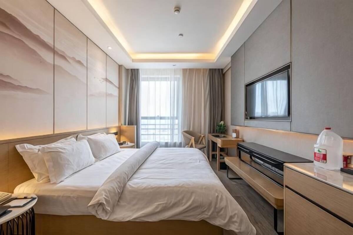 A hotel room with a bed, desk, chair, TV, and a large window.