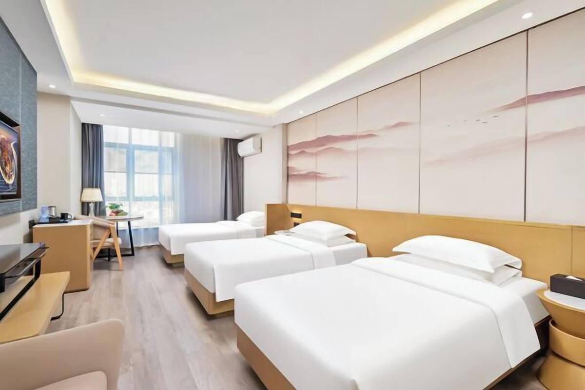 A hotel room with three beds, a desk, a chair, and a large window.