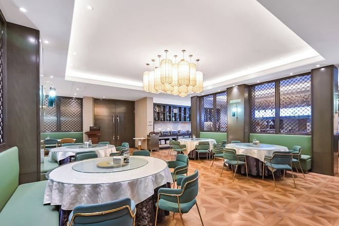 A modern restaurant with round tables, green upholstered seating, and a patterned floor.