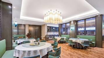 A modern restaurant with round tables, green upholstered seating, and a patterned floor.