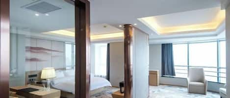 A hotel room with a bed, a desk, a chair, a lamp, and a large window.