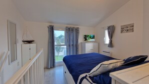 Een slaapkamer met een bed, een televisie, een kledingkast en een raam met gordijnen.