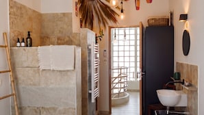 A modern bathroom with a bathtub, shower, and sink, wooden floor, and a view to the living area. - Maison Simone, cosy and private garden - Centre Arles - 2 bedrooms. (Arles)