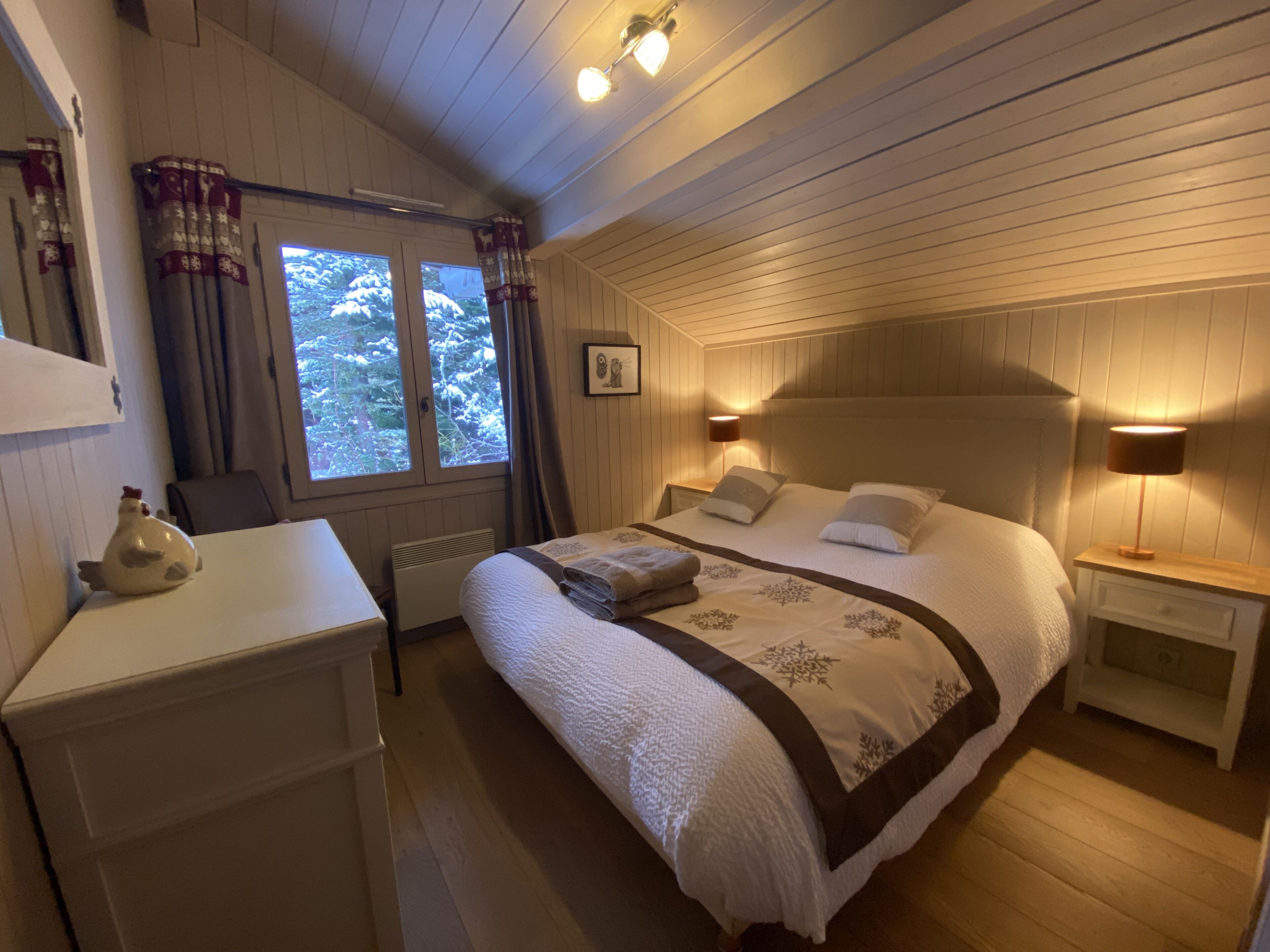 Um quarto aconchegante com cama, mesas de cabeceira, cômoda e janela com cortinas.