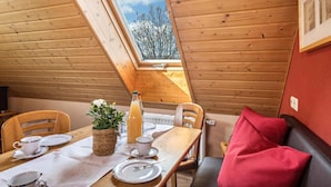 A dining area with a wooden table, chairs, and a red couch. A window with a view of trees is visible. - Ferienhof-Dachsberg Apartment Maisonette (Bermatingen)
