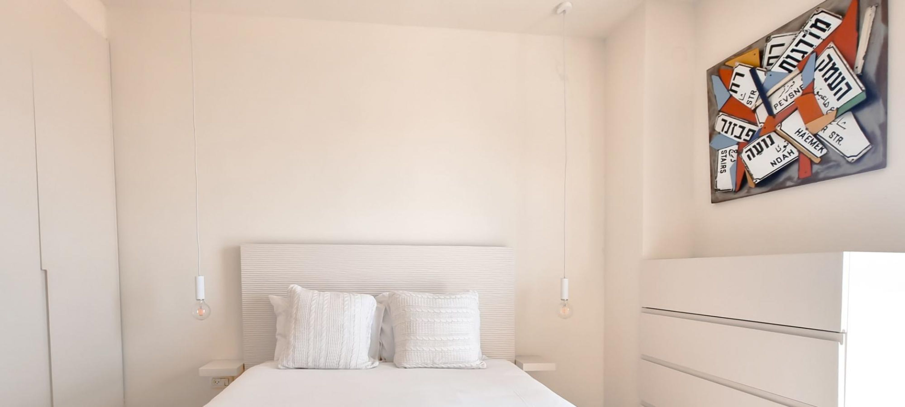 A bedroom with a bed, two pillows, a headboard, and a wall art piece.