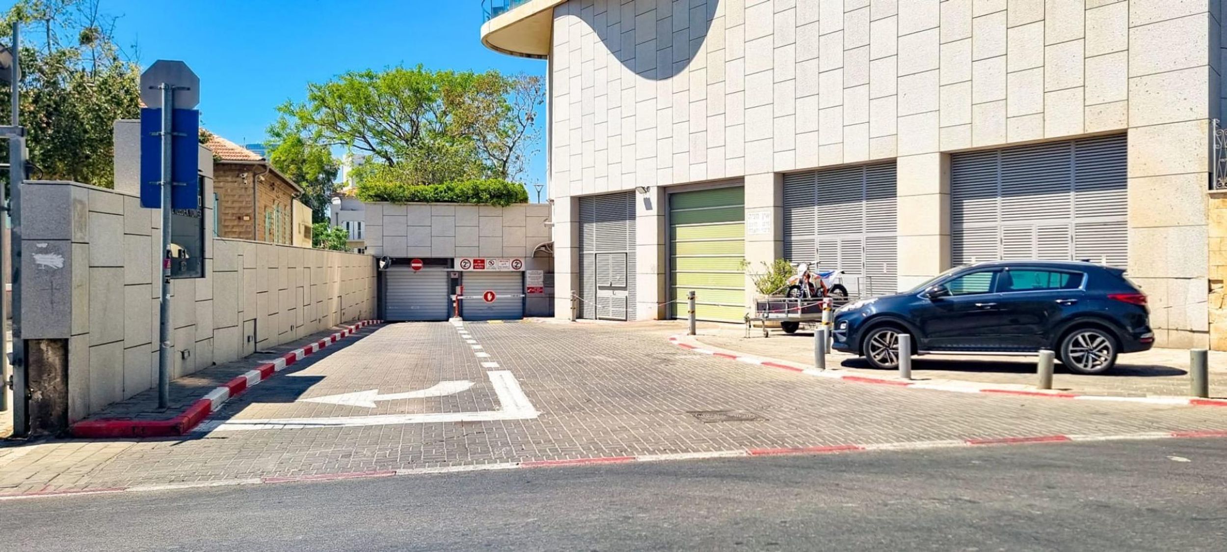 A gated entrance with a blue car parked inside, a building with closed shutters, and a clear sky.