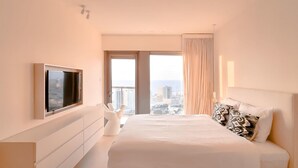 Een moderne hotelkamer met een groot bed, een flatscreen televisie aan de muur, een dressoir en uitzicht op de stad door een groot raam.