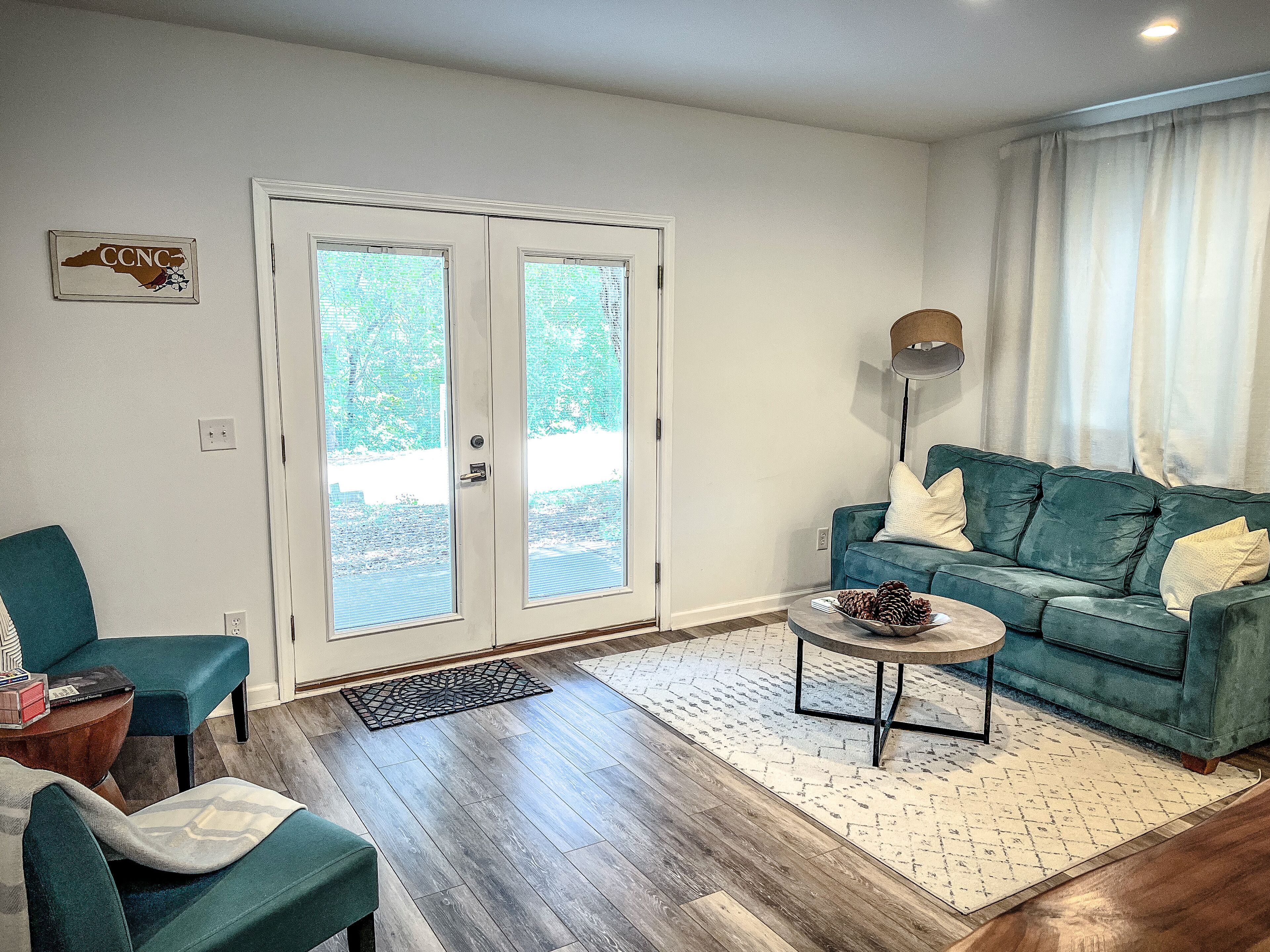 A living room with a teal sofa, a coffee table, and a door leading to a balcony.