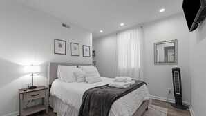 A bedroom with a bed, bedside table, lamp, and a standing heater.