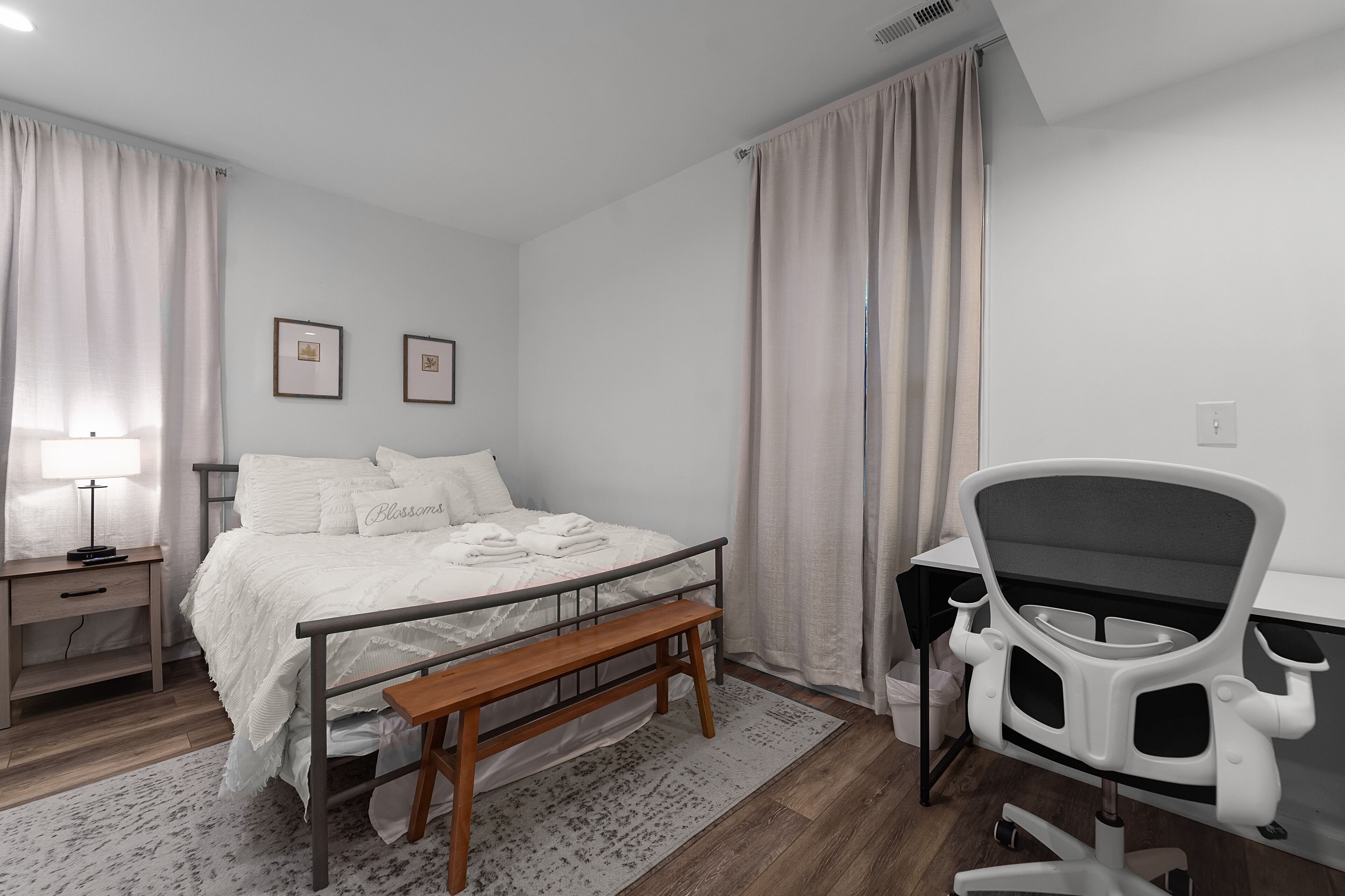 Quarto com cama, mesa de cabeceira, luminária, escrivaninha, cadeira e cortinas.