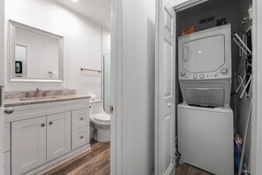Un baño moderno con tocador, lavabo y espejo blancos. Incluye inodoro y lavadora-secadora incorporada.