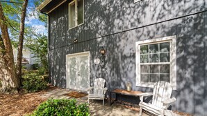 A wooden house with two white Adirondack chairs and a small table outside.