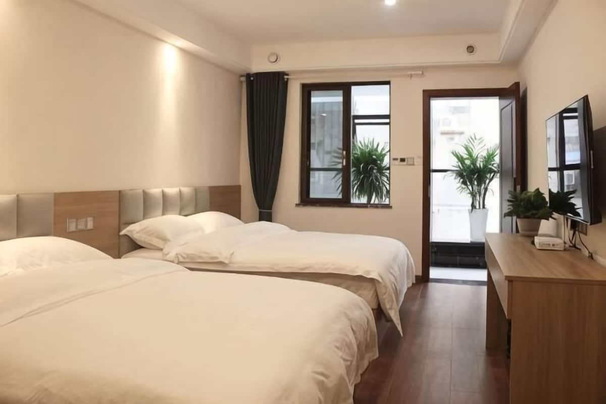 A hotel room with two beds, a desk, a TV, and a window with a view.