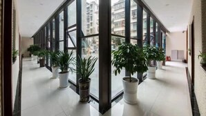 Un pasillo amplio con ventanas grandes, plantas en macetas y vistas de edificios.
