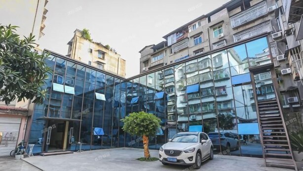 Un edificio moderno con fachada de vidrio, un coche estacionado y un pequeño árbol en primer plano.