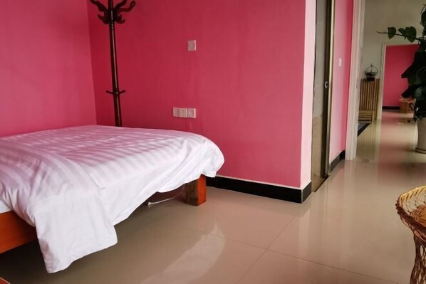 Une pièce avec un lit, un plancher en bois et un mur rose.