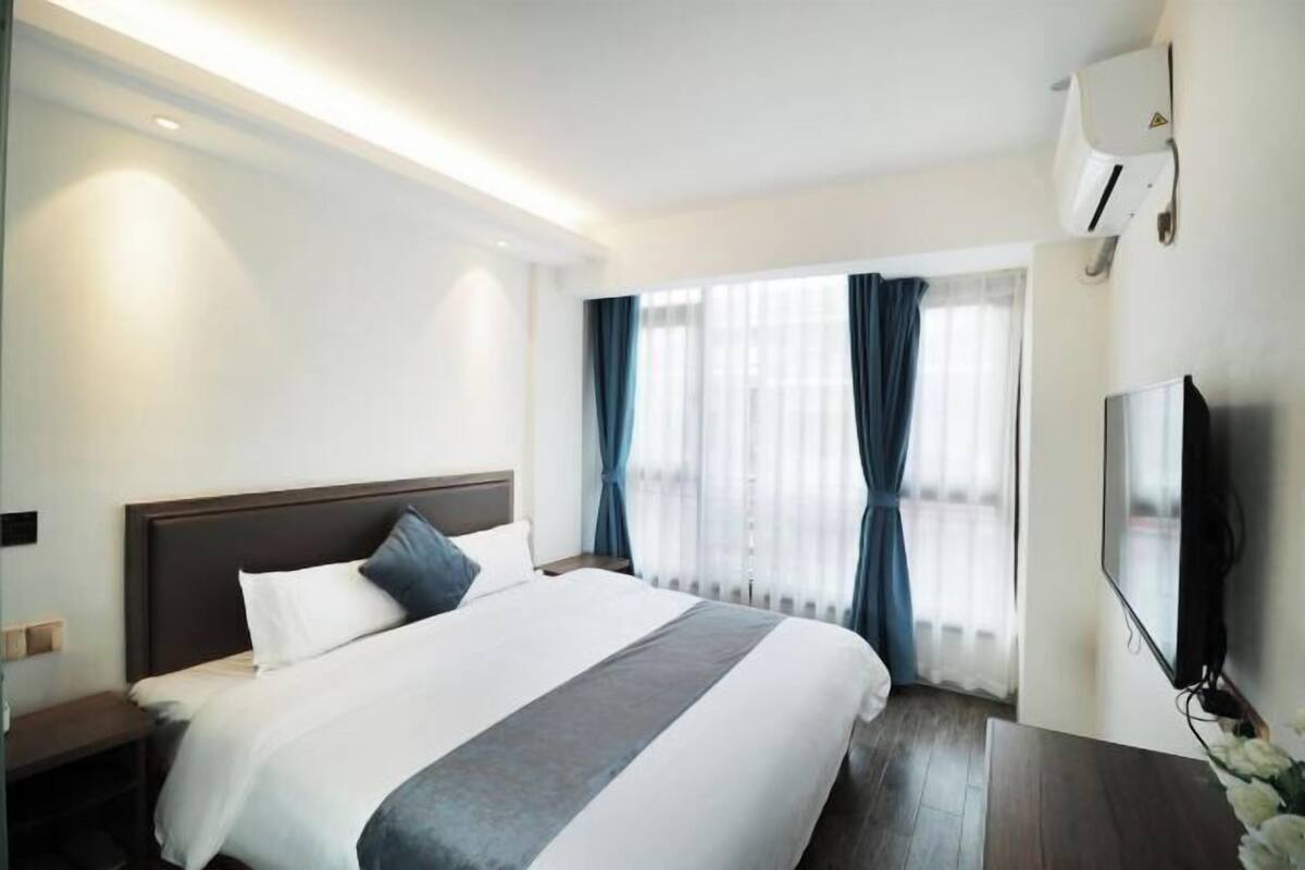 A hotel room with a large bed, a bedside table, a TV, and a window with curtains.