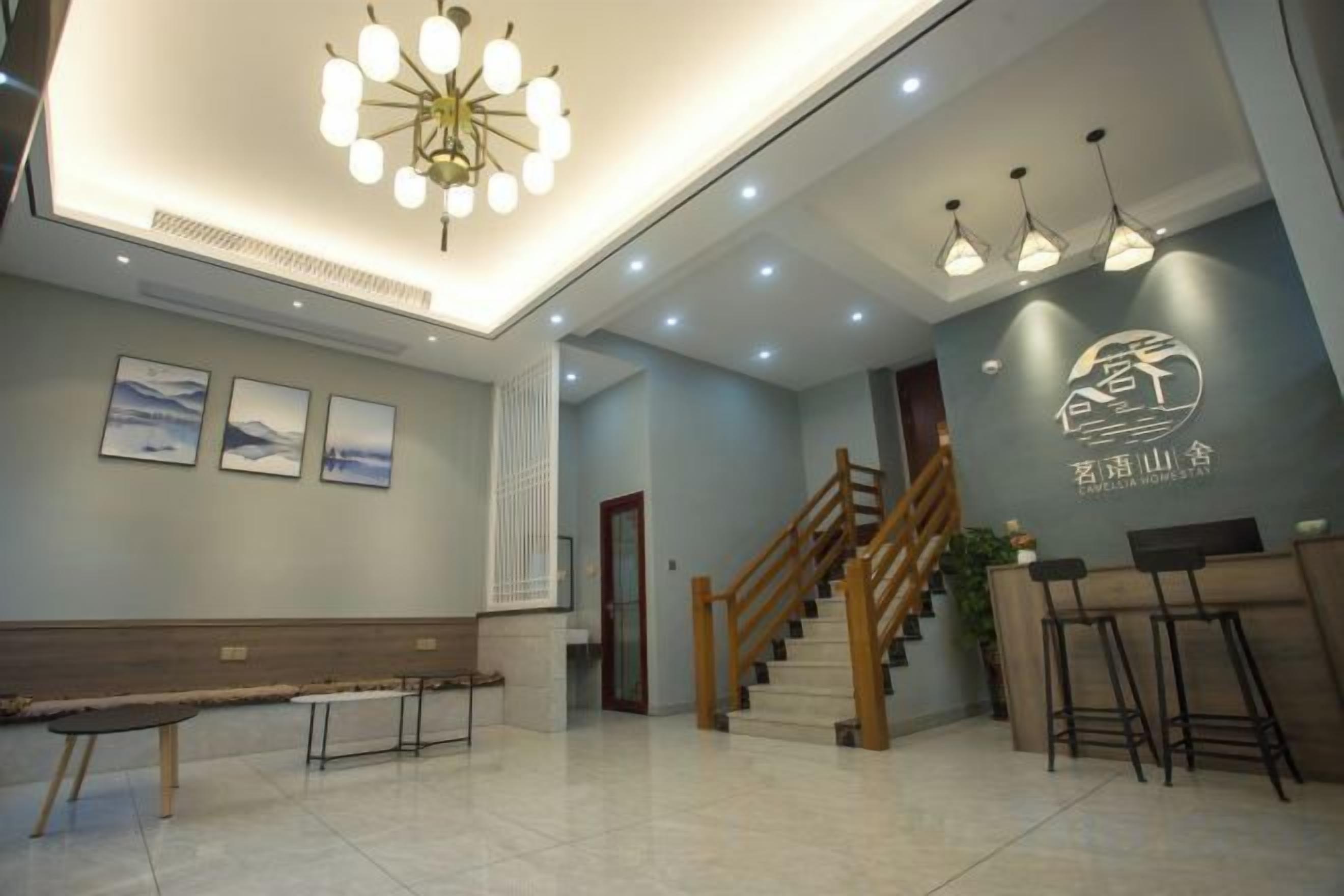 Rebedor d'hotel amb taulell de recepció, una banca de fusta, unes escales i un penjall.