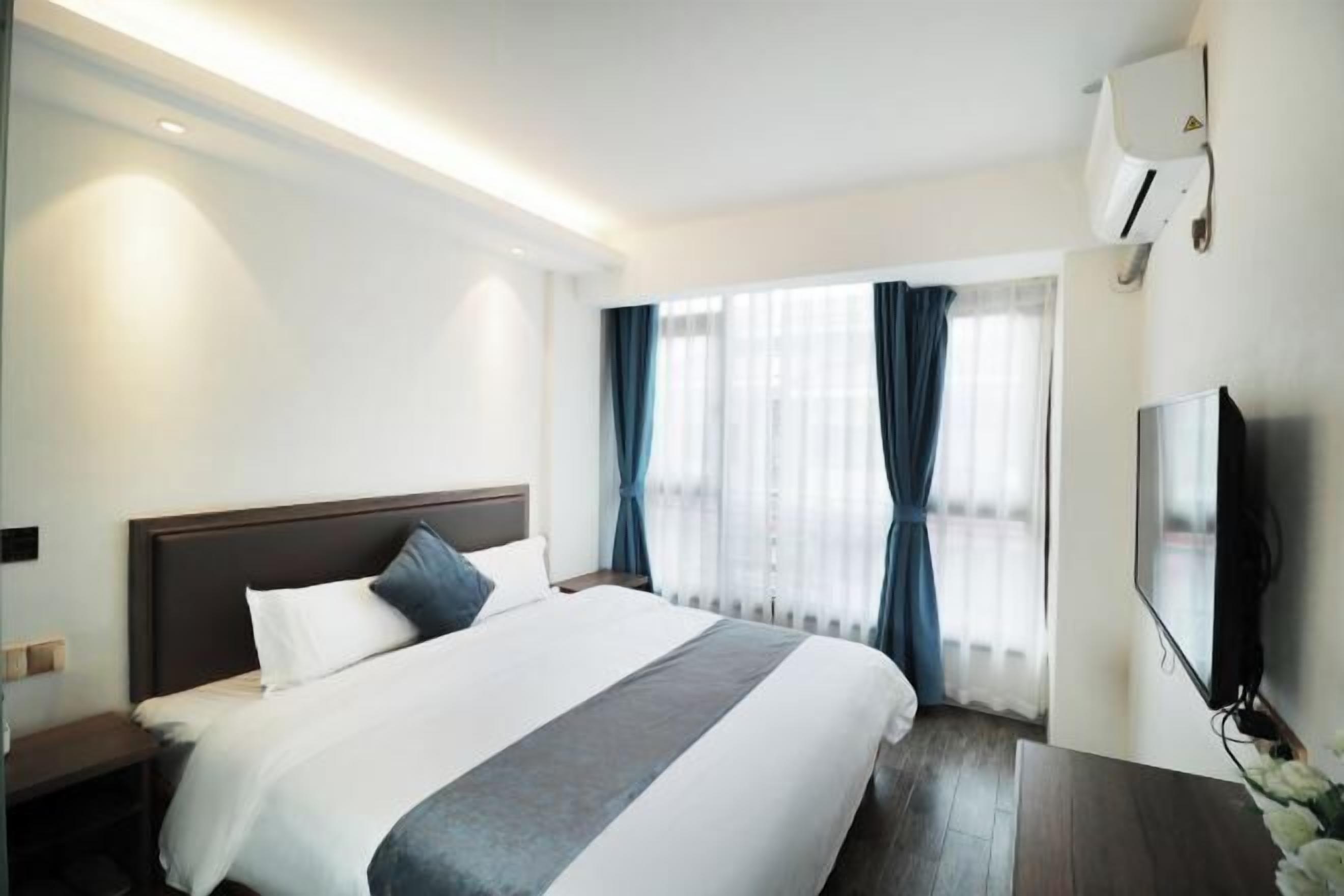 A hotel room with a large bed, a bedside table, a TV, and a window with curtains.