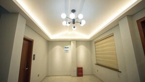 A hallway with a modern ceiling light fixture, a door on the left, and a window with blinds on the right. - Mingyu Shanshe Hostel (Wuyishan)