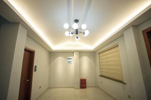 A hallway with a modern ceiling light fixture, a door on the left, and a window with blinds on the right. - Mingyu Shanshe Hostel (Wuyishan)