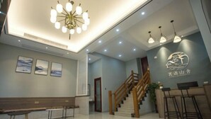 A modern hotel lobby with a reception desk, wooden staircase, and a bench. - Mingyu Shanshe Hostel (Wuyishan)