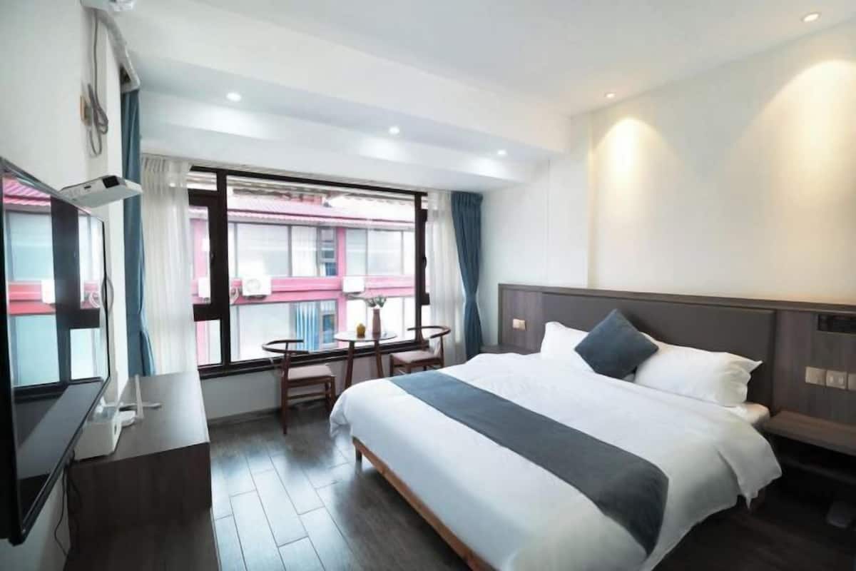 A hotel room with a bed, bedside table, TV, and a window with curtains.