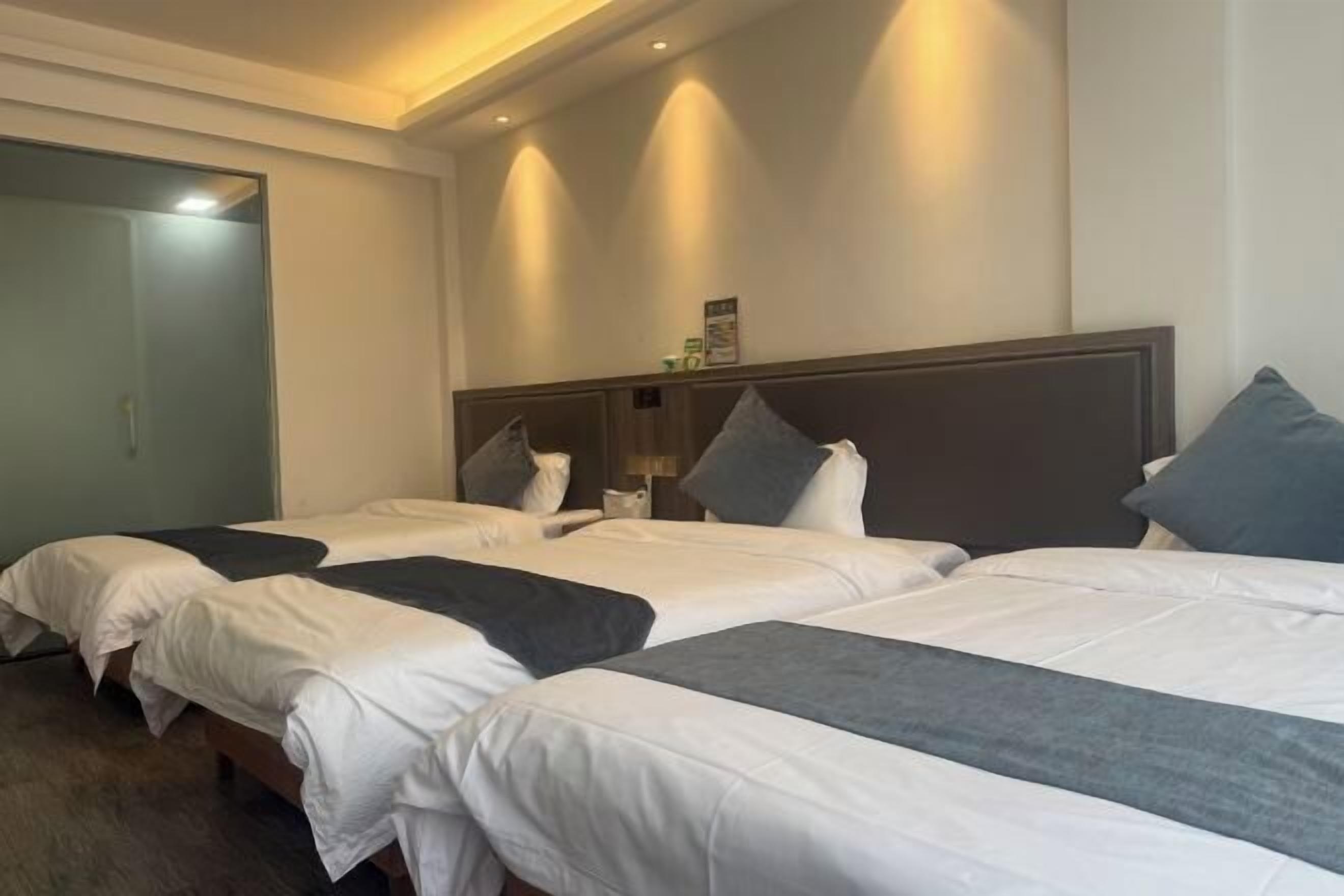A hotel room with three single beds, a wooden headboard, and a small bedside table with a lamp.