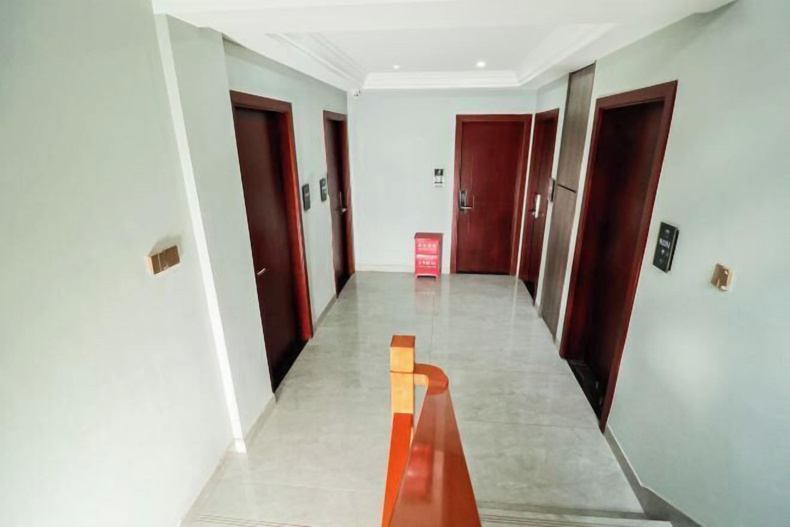 Un pasillo de diseño moderno, con un banco rojo central, paredes de colores claros y puertas de madera.