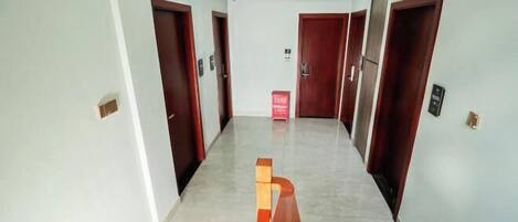 Un pasillo de diseño moderno, con un banco rojo central, paredes de colores claros y puertas de madera.