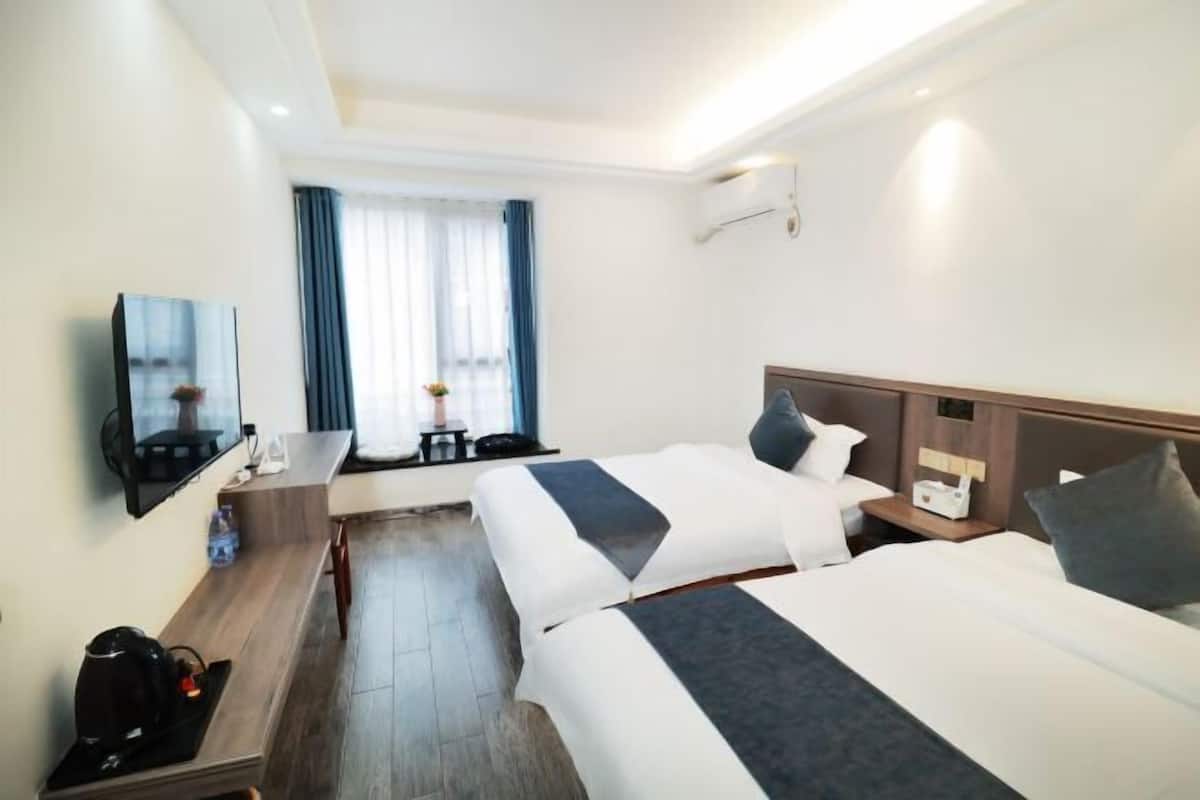 A hotel room with two beds, a desk with a coffee maker, a TV, and a window with curtains.