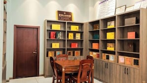 A room with a wooden table and chairs, surrounded by wooden bookshelves filled with books. - Mingyu Shanshe Hostel (Wuyishan)