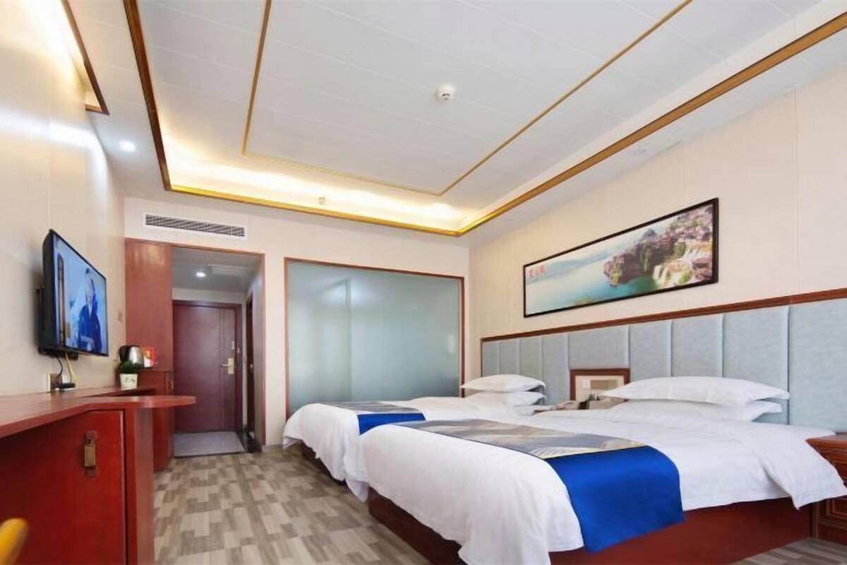 A hotel room with a bed, a desk, a television, and a painting on the wall.