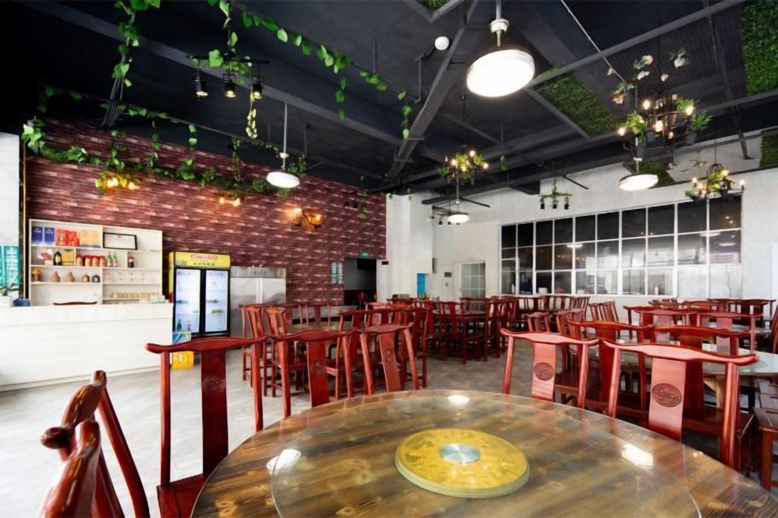 A restaurant interior with round tables, red chairs, hanging plants, and brick walls.