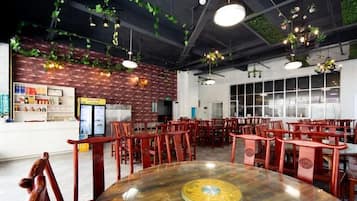 A restaurant interior with round tables, red chairs, hanging plants, and brick walls.