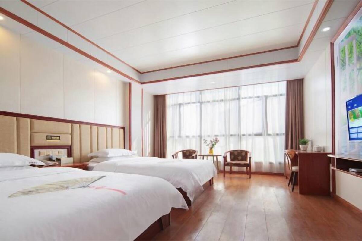 A hotel room with two beds, a desk, a chair, and a large window with curtains.