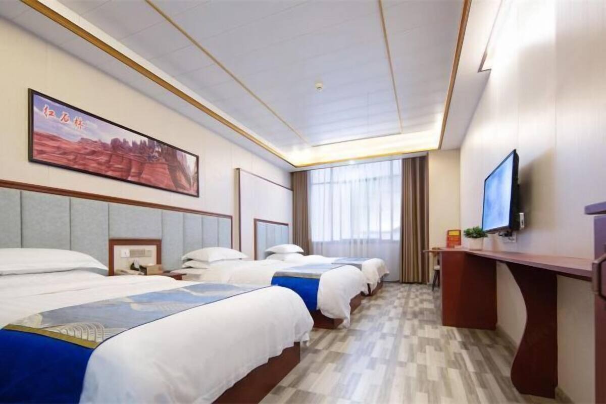 A hotel room with four beds, a desk, a television, and a large painting on the wall.