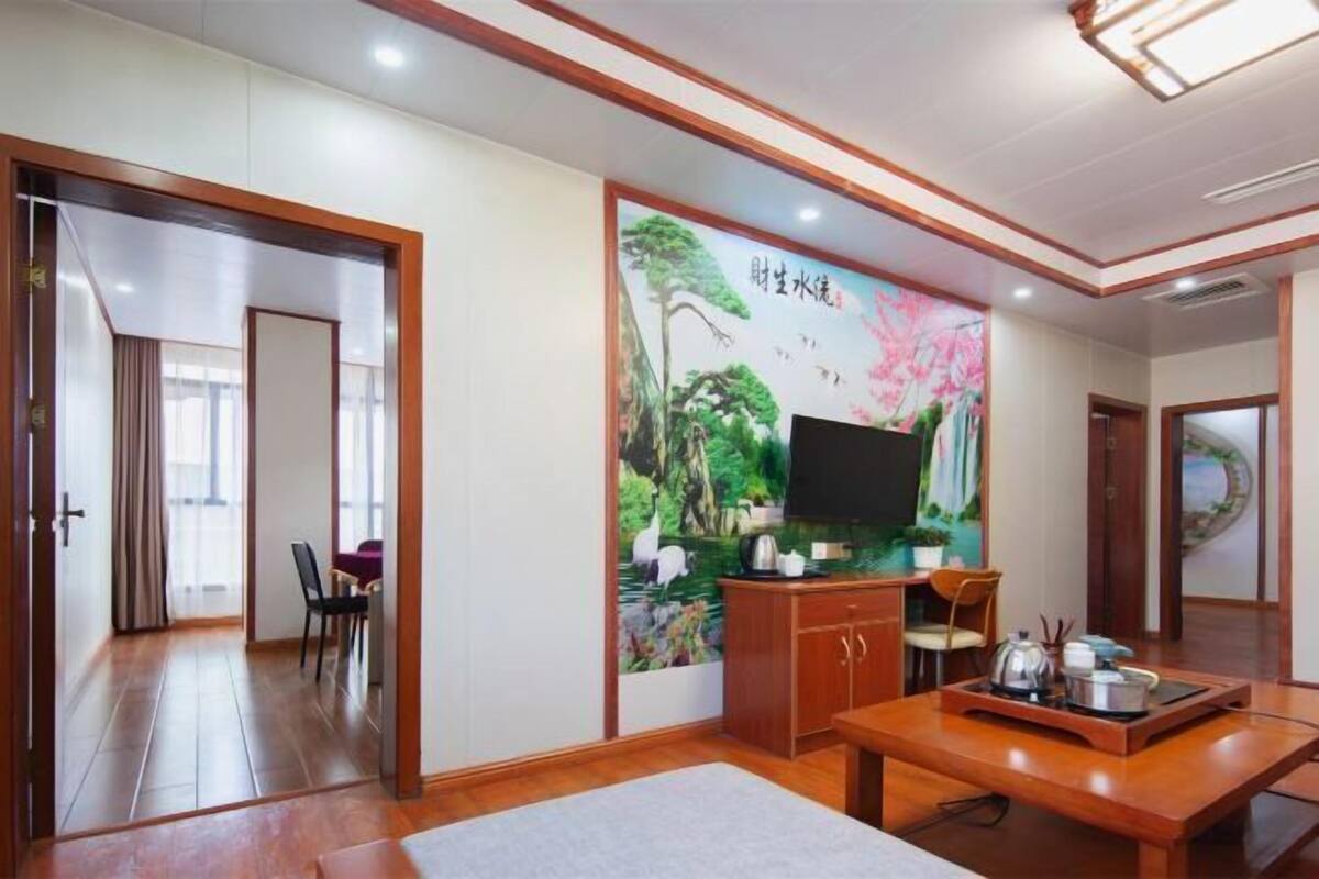 A room with a TV, wooden furniture, a painting, and a view of a corridor.