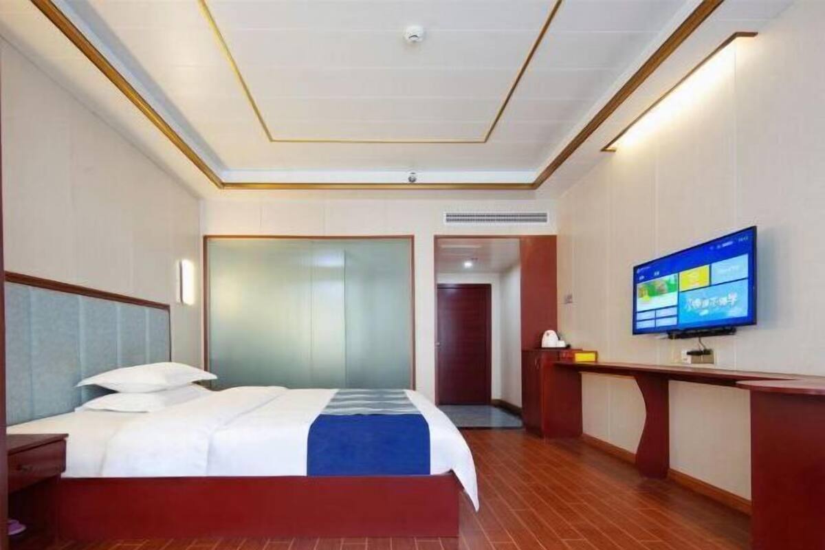 A hotel room with a bed, a TV, a desk, and a door leading to another room.