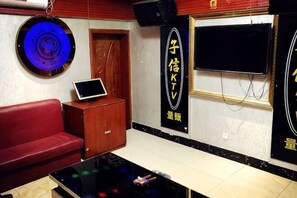 A room with a red sofa, a small wooden cabinet, a black table with a glass top, a wall-mounted TV, and a circular light fixture. - Zixin Space Leisure Hotel (Yulong)