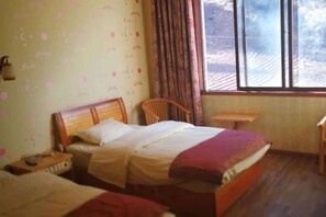 Un dormitorio con dos camas, una ventana con cortinas, una silla de madera y una mesita.