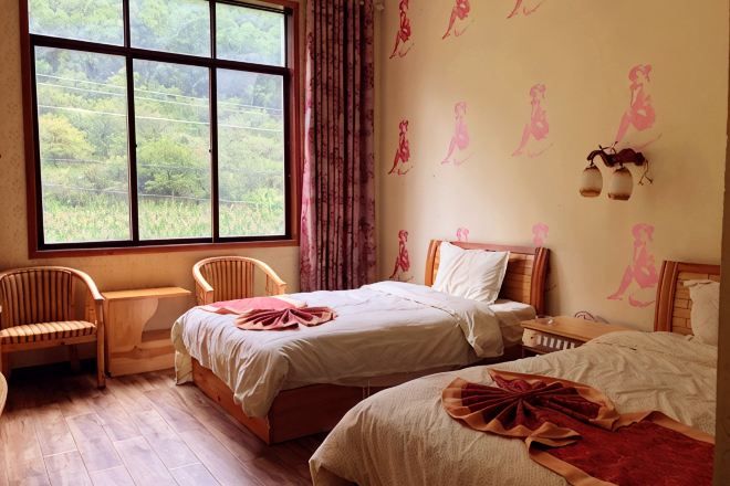 Une chambre avec deux lits, une fenêtre donnant sur un beau paysage, une chaise et un mur agrémenté d’éléments décoratifs.